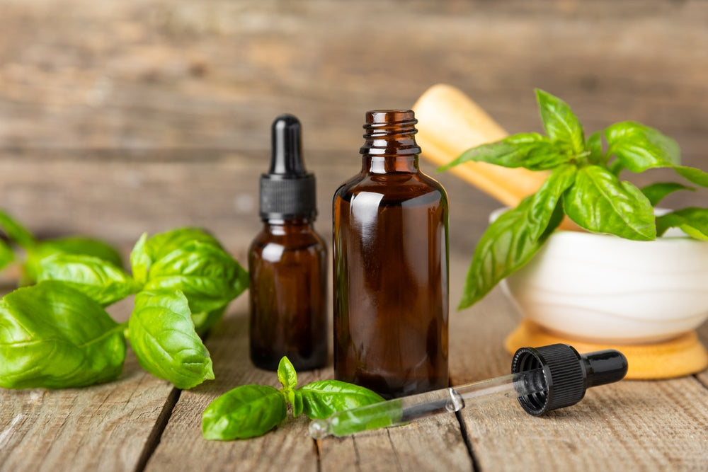 Basil essential oil in a bottle on a textured wooden background with fresh basil leaves