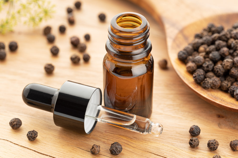 Black pepper essential oil in bottle on wooden table with peppercorns