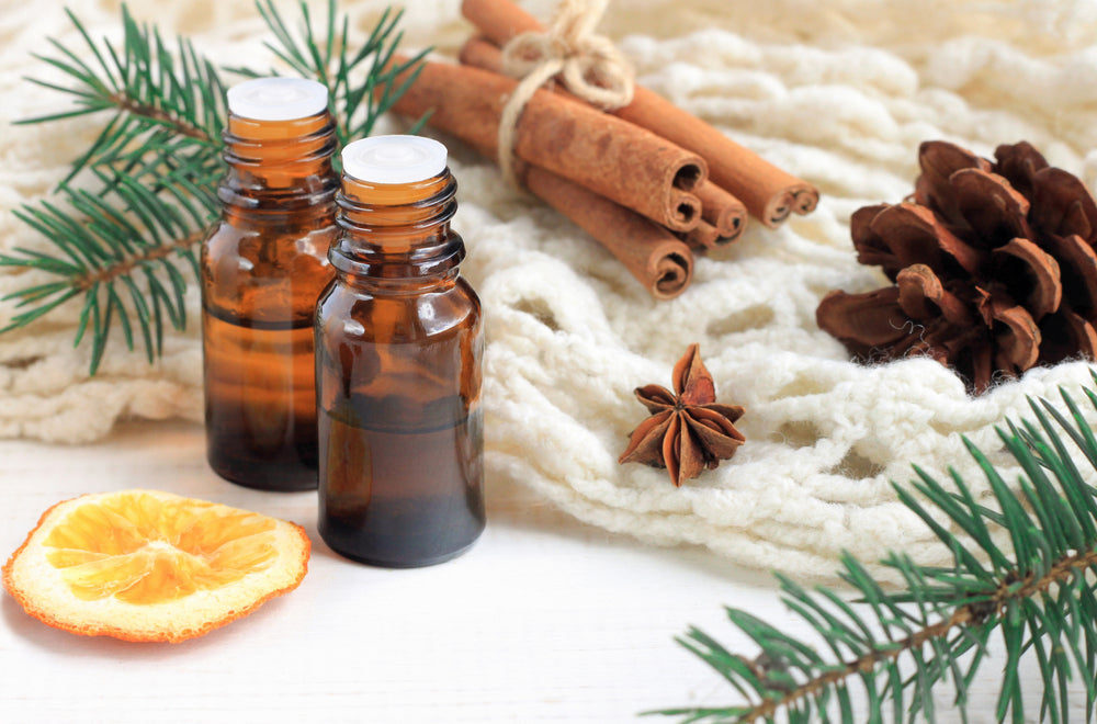 Dark glass therapeutic essential oil bottles by cinnamon, pine twigs, dried citrus slice, anise, and a woolen wrap