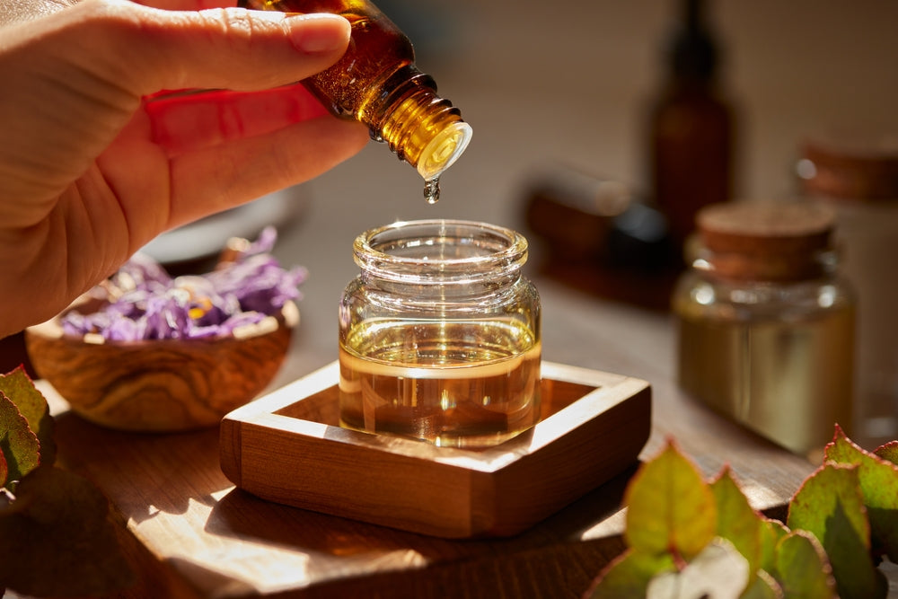hand pouring essential oil into a jar on a cluttered table