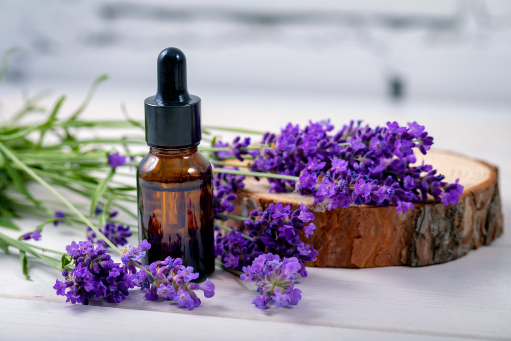 lavender essential oil in bottle by lavender flowers and log slice