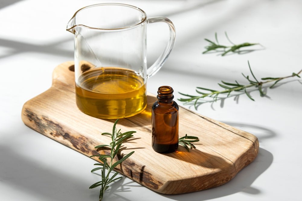 pitcher of carrier oil by bottle of essential oil on wooden cutting board