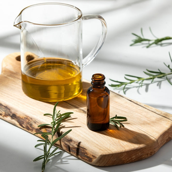 pitcher of carrier oil by bottle of essential oil on wooden cutting board