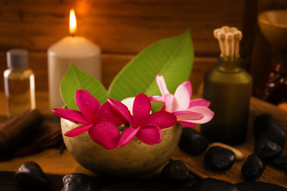 Frangipani flowers in bowl with essential oil and a lit candle with spa supplies