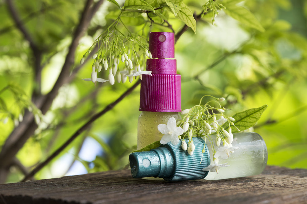 two bottles of essential oil room spray by a blooming tree outside