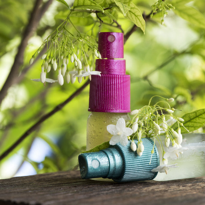 two bottles of essential oil room spray by a blooming tree outside