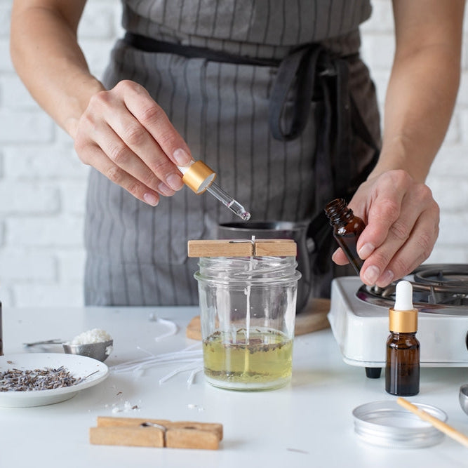 woman with apron adding essential oil to a candle she is making