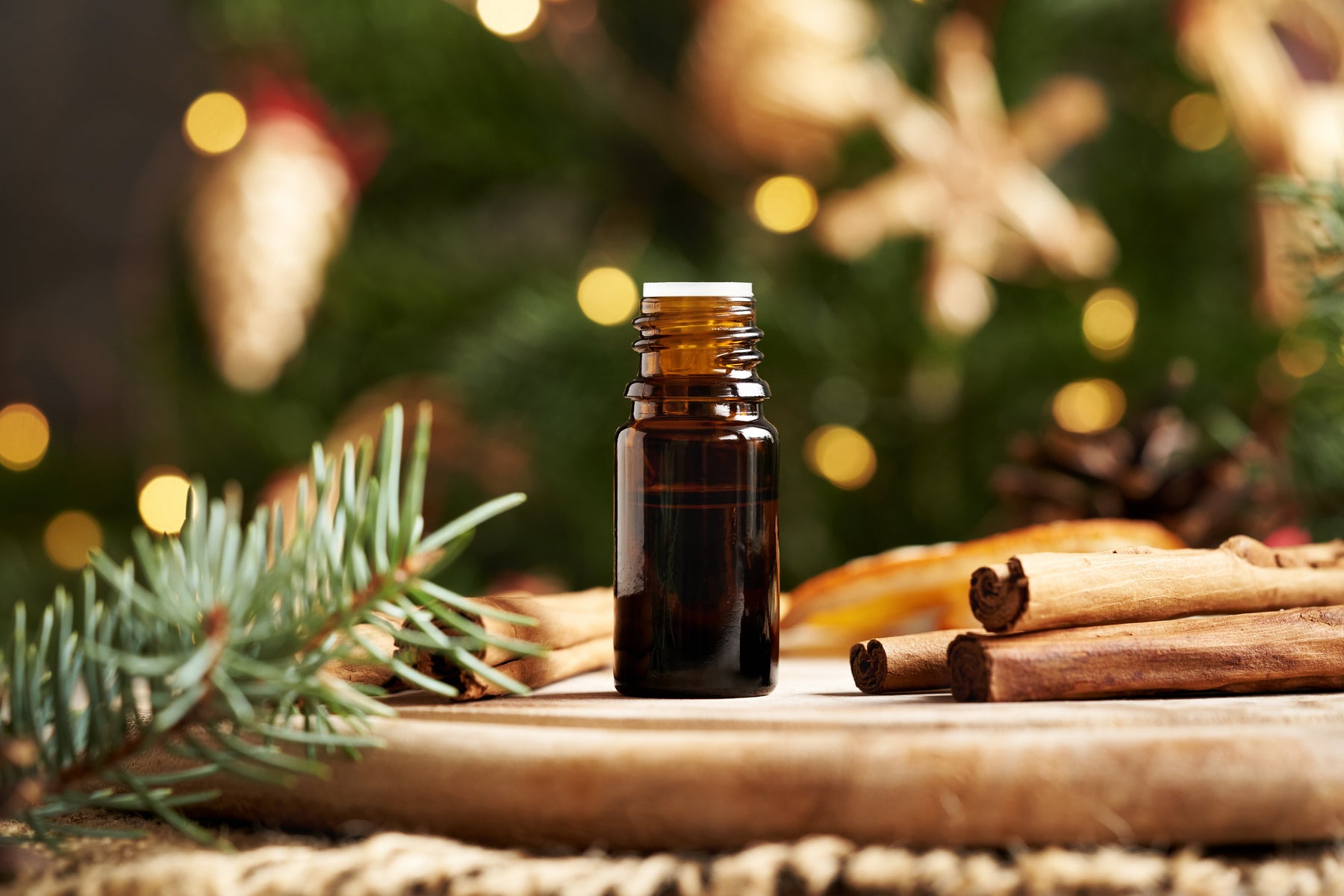 A bottle for a Christmas essential blend next to evergreen and cinnamon sticks.