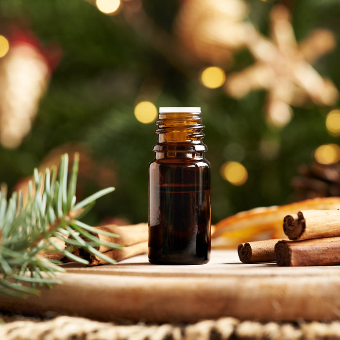 A bottle for a Christmas essential blend next to evergreen and cinnamon sticks.