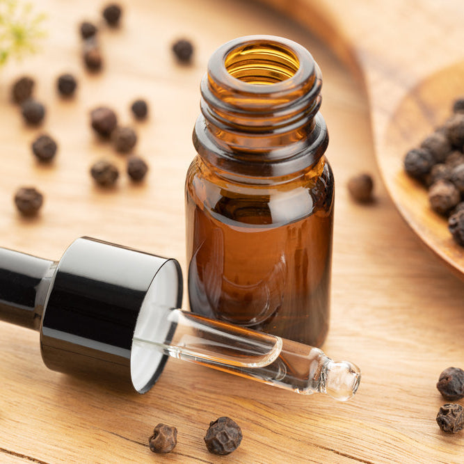 Black pepper essential oil in bottle on wooden table with peppercorns