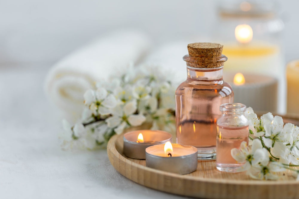 Spa products, aromatherapy, atmosphere of relax. Candles and spa essentials on bamboo tray in bathroom, essential oil, bath salt, towel, sea stone, spring apple tree blooming flowers
