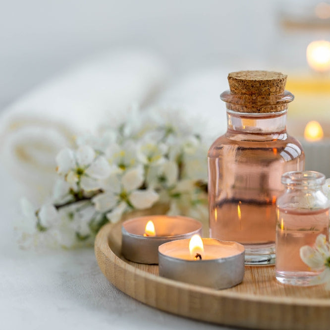 Spa products, aromatherapy, atmosphere of relax. Candles and spa essentials on bamboo tray in bathroom, essential oil, bath salt, towel, sea stone, spring apple tree blooming flowers