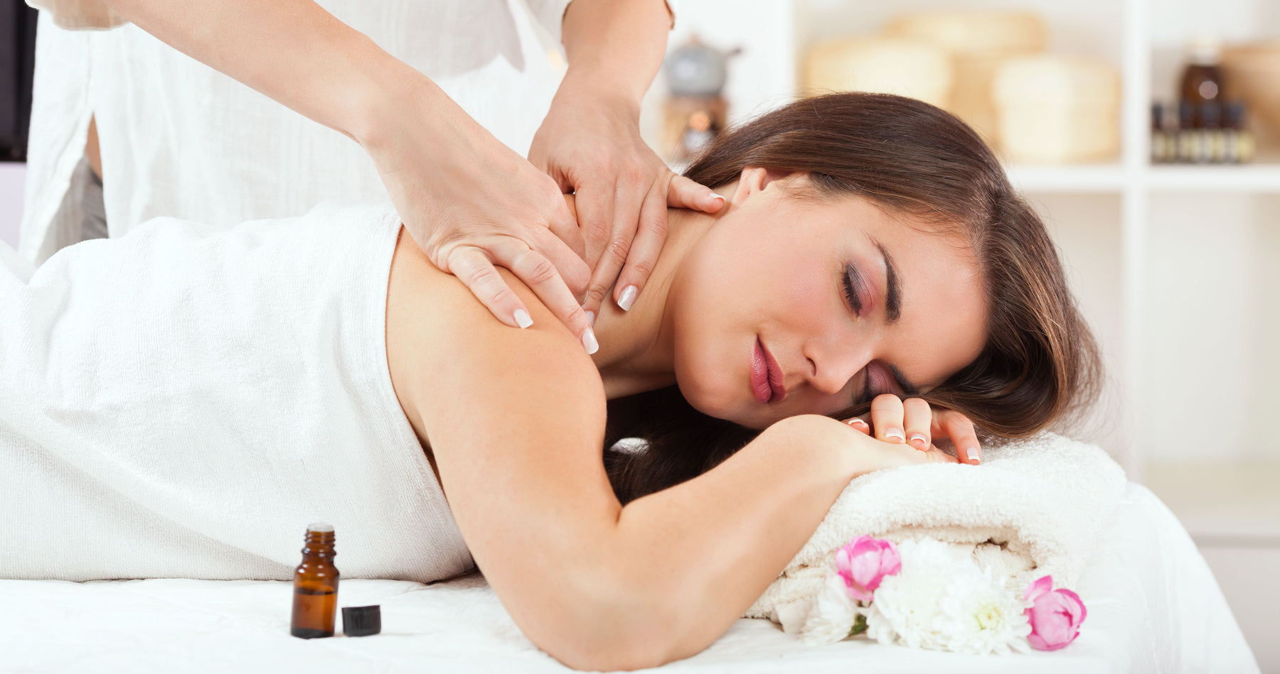 woman being massaged with essential oil bottle next to her