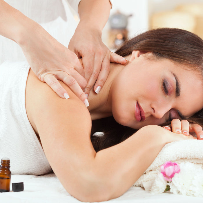 woman being massaged with essential oil bottle next to her