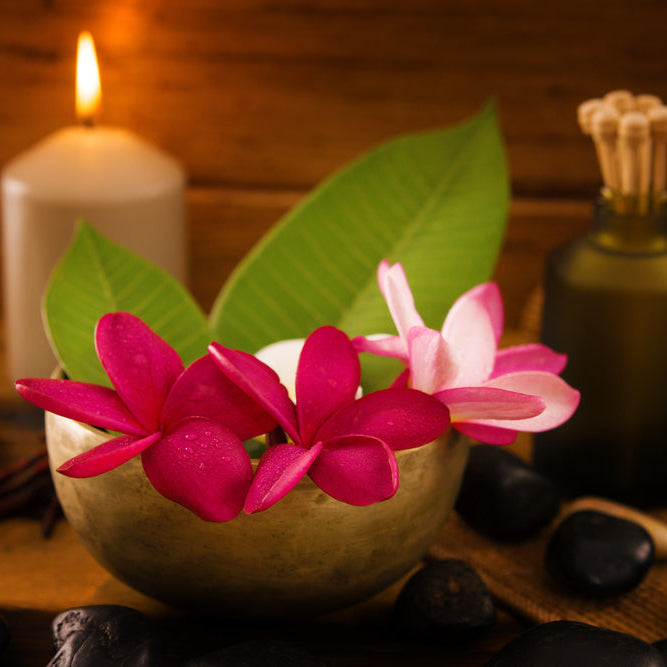 Frangipani flowers in bowl with essential oil and a lit candle with spa supplies