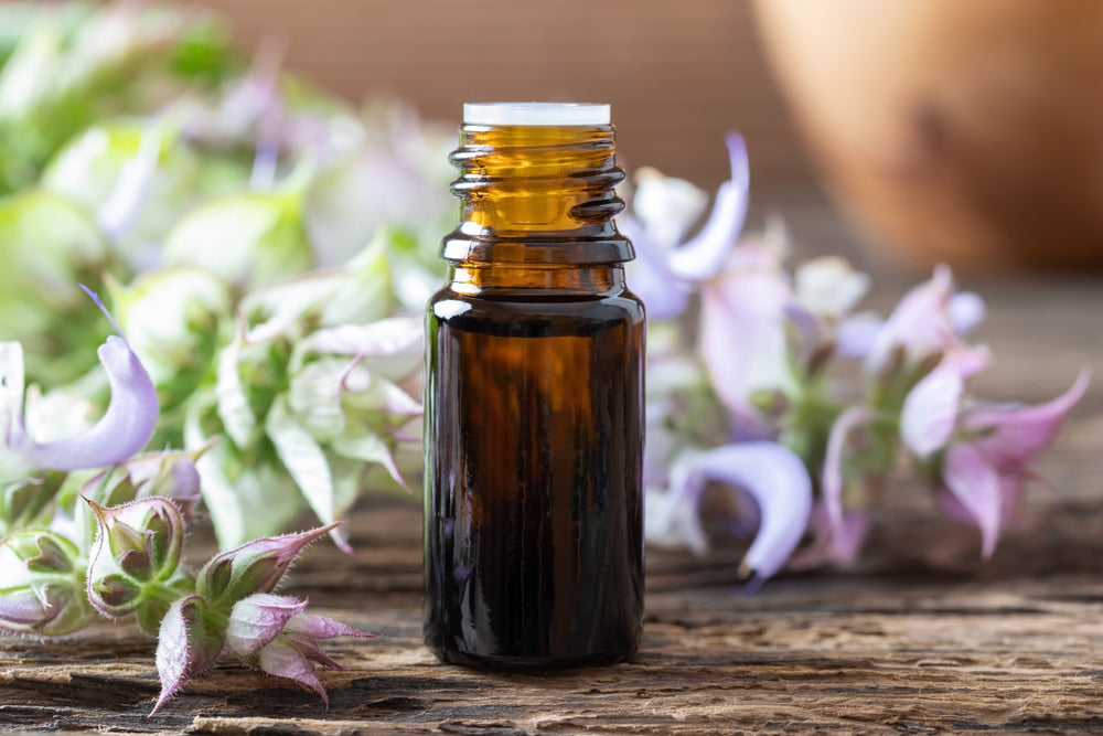 bottle of clary sage essential oil in front of clary sage blooms on wooden table