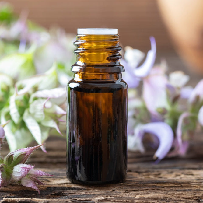 bottle of clary sage essential oil in front of clary sage blooms on wooden table