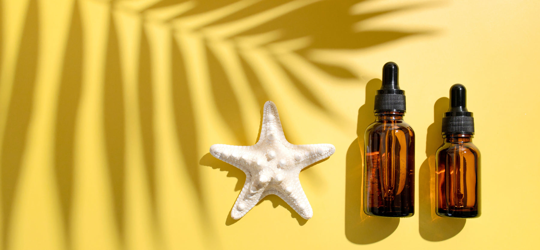 two bottles of essential oils on yellow sand with starfish