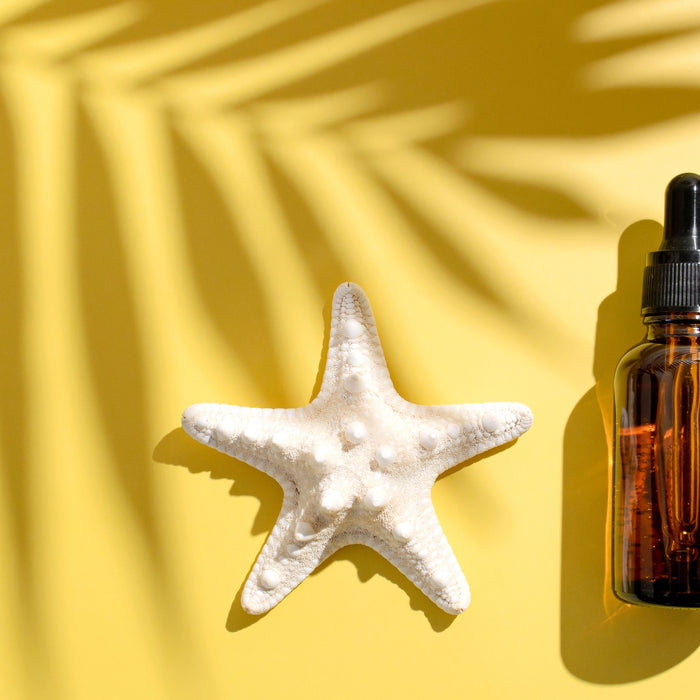 two bottles of essential oils on yellow sand with starfish