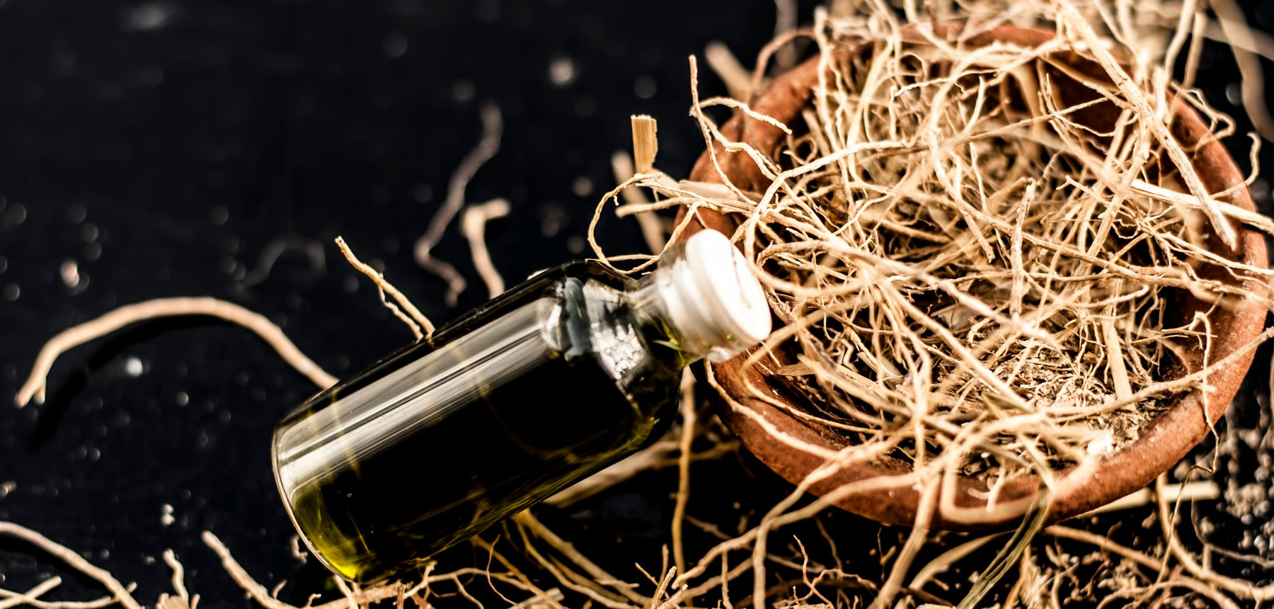 bottle of vetiver essential oil on pile of dried vetiver